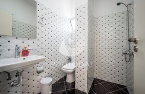 Casa de banho com lavatório branco, sanita e chuveiro. As paredes apresentam um padrão de mosaicos em forma de losango.