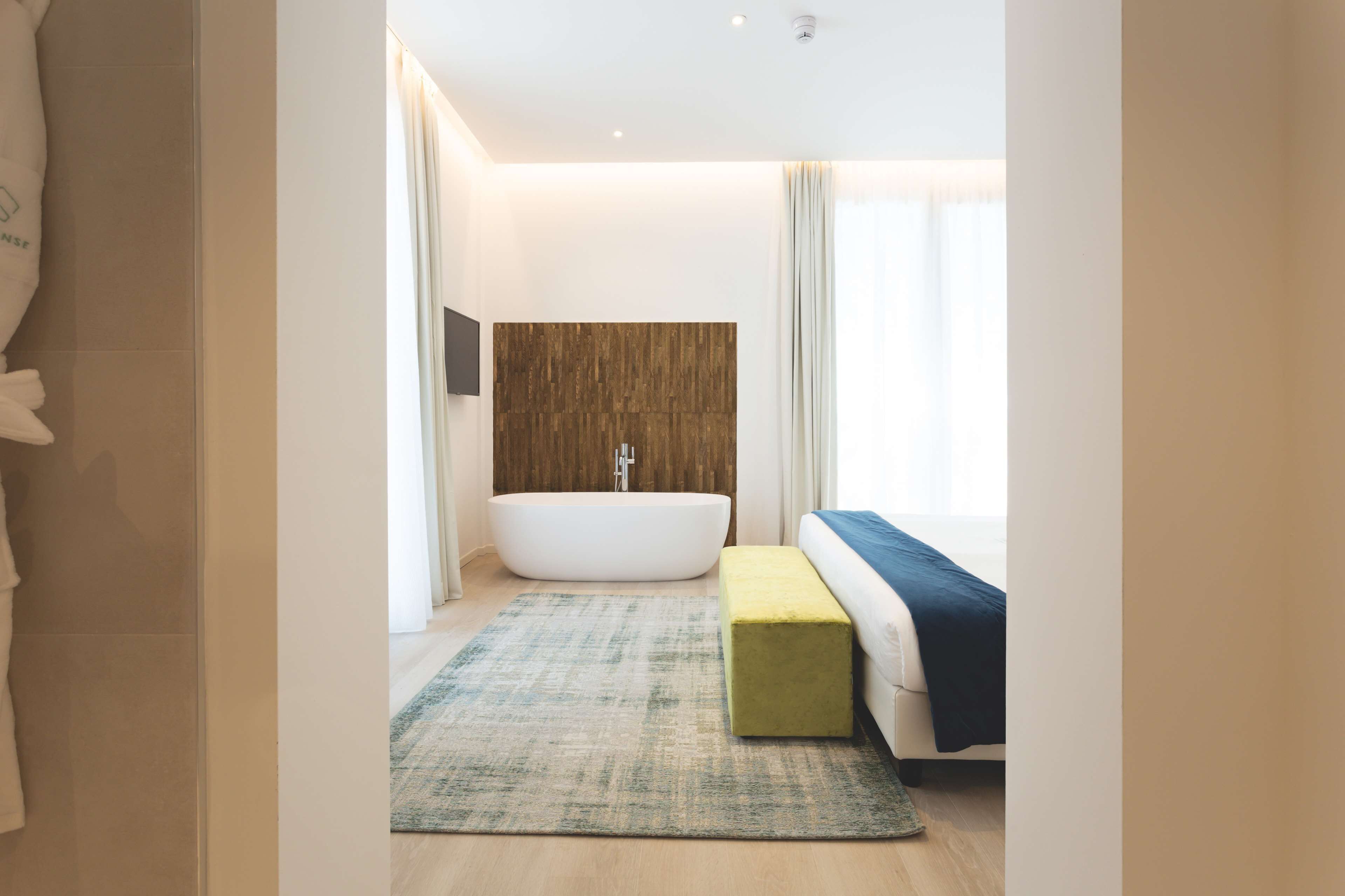 A modern bathroom with a freestanding bathtub, a wooden accent wall, and a large window providing natural light.