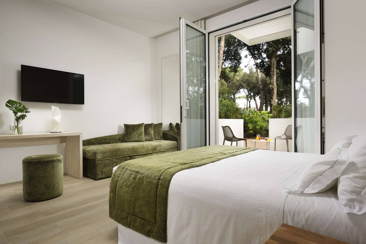 A modern bedroom with a bed, a sofa, and a TV on a wall.