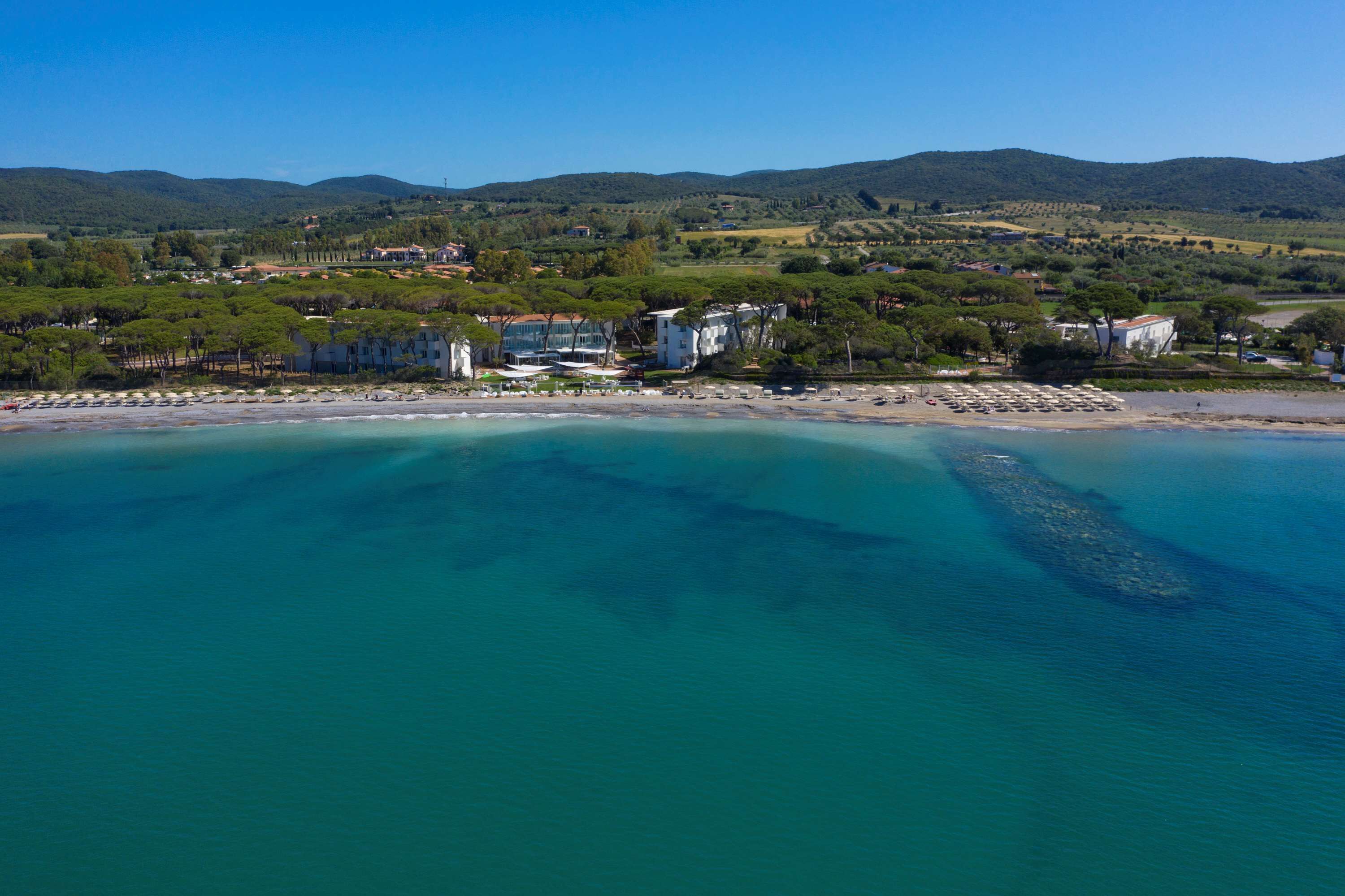 An aerial view of a coastal area with buildings, a beach, and a clear blue sea.