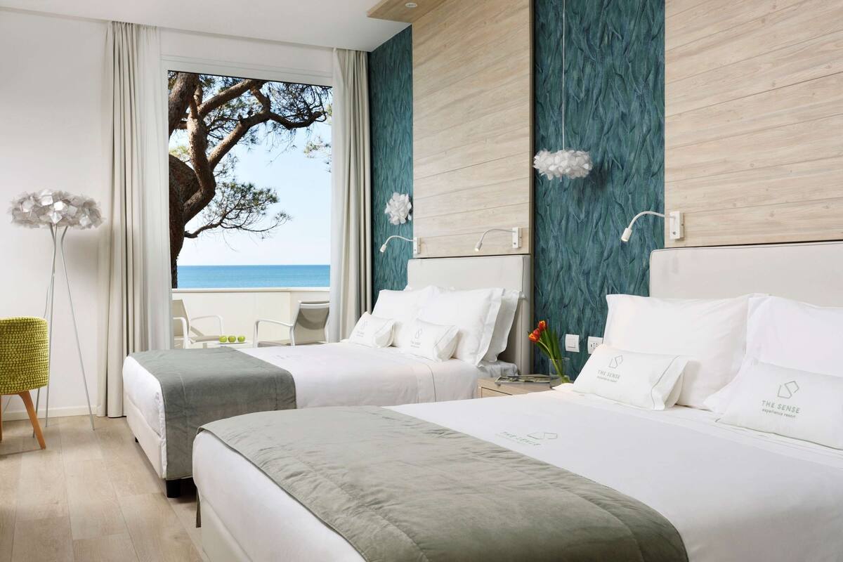 A hotel room with two beds, a view of the sea, and a modern design with teal and wooden accents.