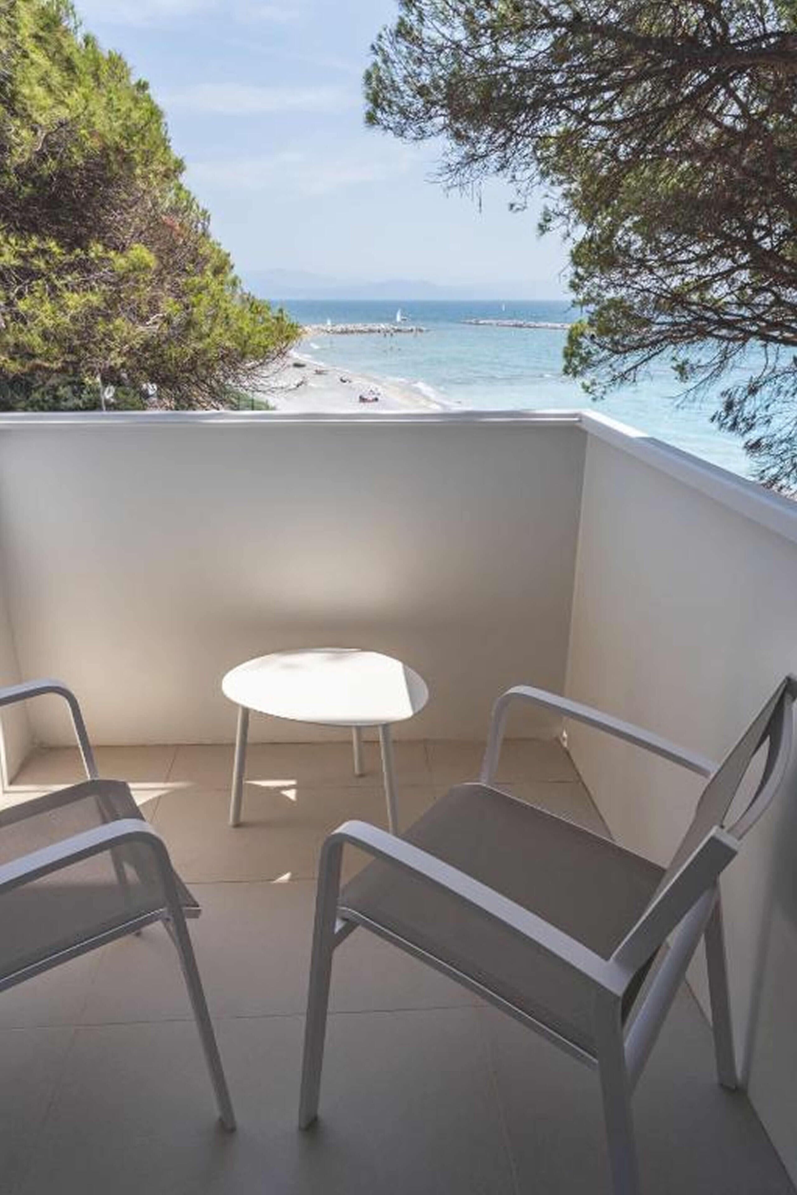 Ein Balkon mit zwei Metallstühlen und einem kleinen runden Tisch, mit Blick auf einen Strand und das Meer.