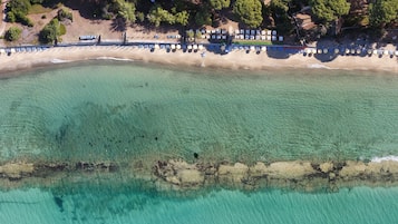 Vista aerea di una spiaggia con acque turchesi cristalline, un litorale sabbioso e file di ombrelloni blu.