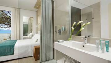 Una habitación de hotel moderna con cama, baño con un espejo grande y artículos de aseo en la encimera.