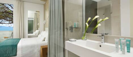 A modern hotel room with a bed, a bathroom with a large mirror, and toiletries on the sink.