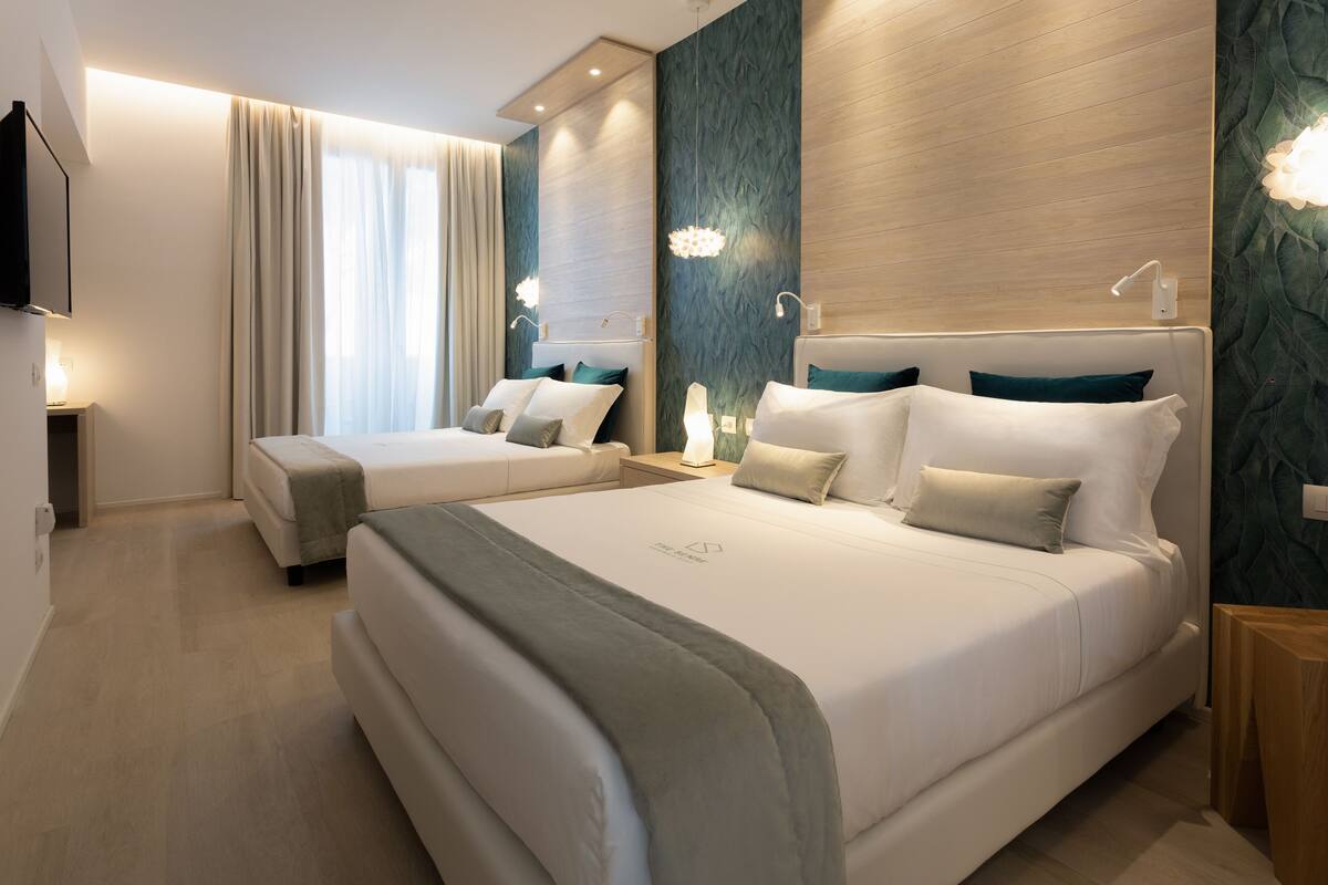 A modern hotel room with two beds, a flat-screen TV, and a large window with curtains.