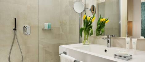 Un baño moderno con cabina de ducha de vidrio, un espejo grande y un jarrón con flores amarillas.