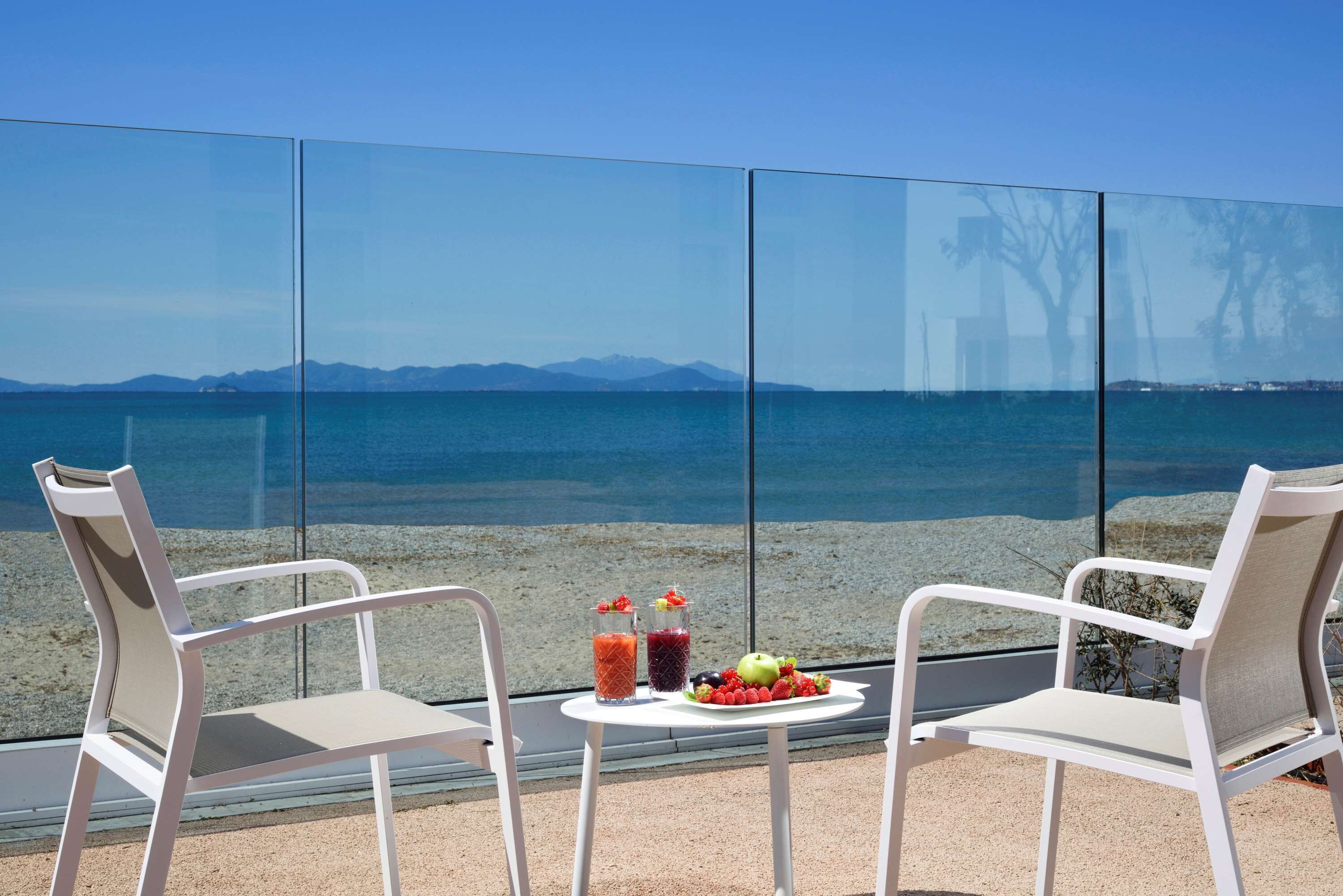 Deux chaises blanches sont placées face à un mur de verre, offrant une vue sur la mer et les montagnes.