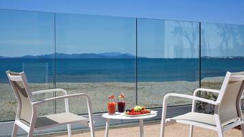 Two white chairs facing a glass wall with a view of the sea and mountains.