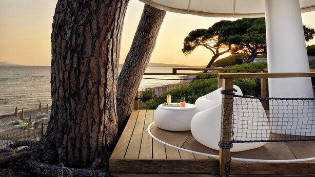 Una terraza de madera con un espacio de estar al aire libre en blanco, una pérgola y vistas al mar.