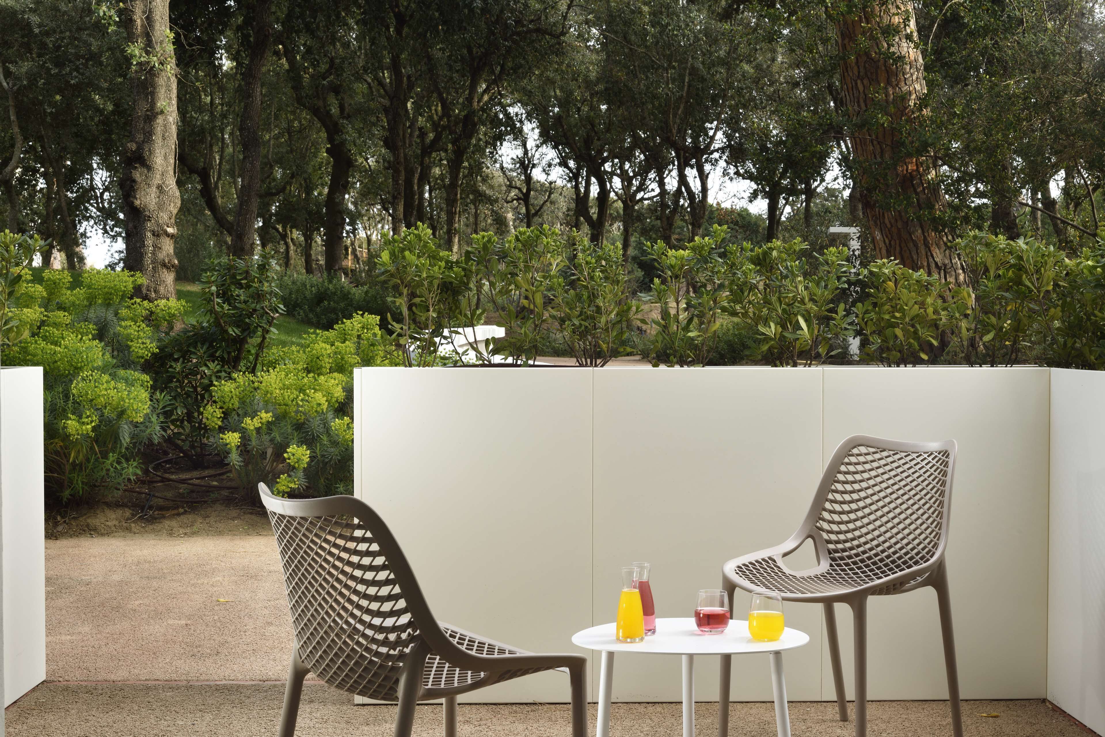 Un espace extérieur aménagé avec deux chaises et une table, entouré d’une végétation luxuriante et d’arbres.