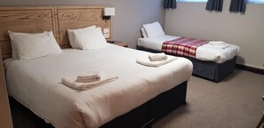 Una habitación de hotel con una cama grande, una cama más pequeña y una mesita de noche con lámpara.