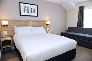 A hotel room with a large bed, two bedside tables with lamps, a dark sofa, and a framed feather artwork on the wall.