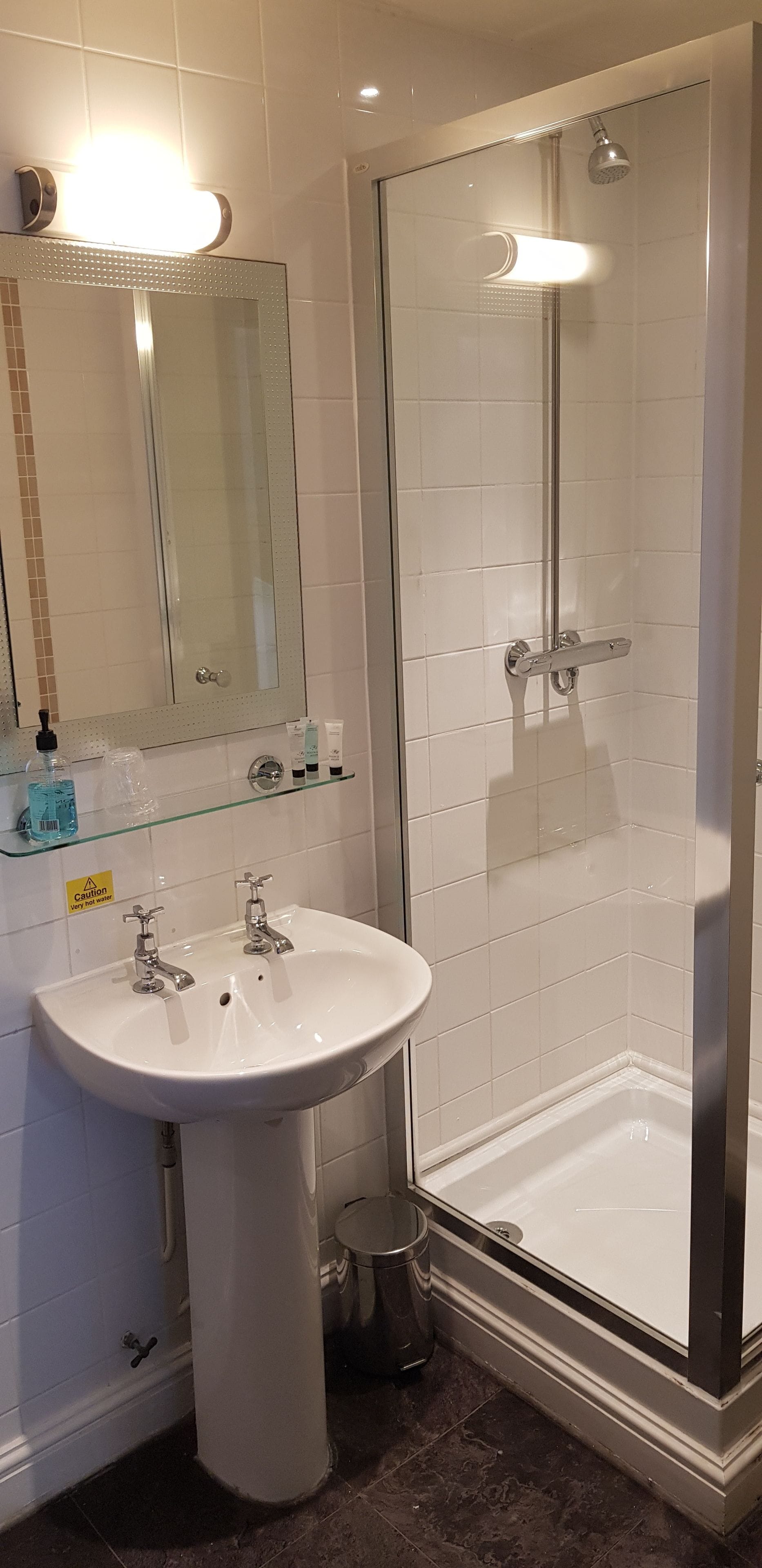 Een badkamer met een wit wastafelmeubel, een glazen douchecabine en een spiegel met verlichting.