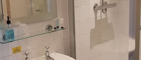 Un baño con lavamanos blanco, cabina de ducha con paredes de vidrio y espejo con iluminación.