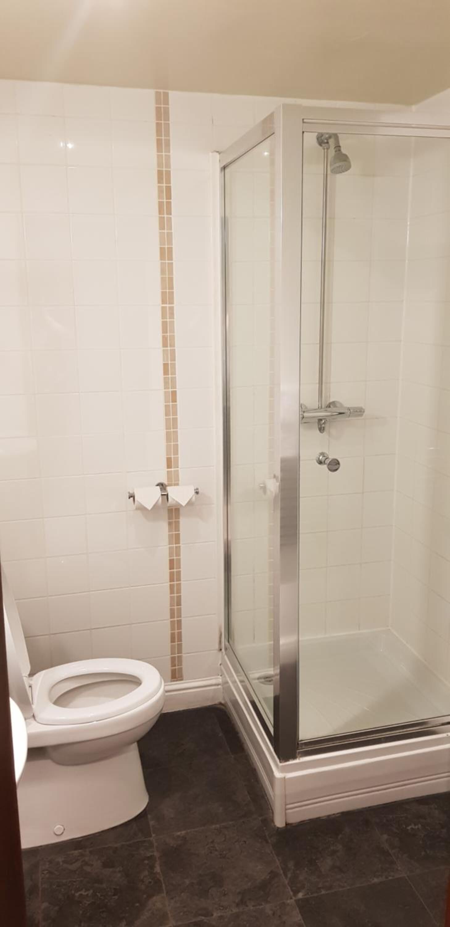 Un baño con inodoro, cabina de ducha de vidrio y pared con un listón vertical color beige.