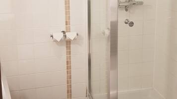 Un baño con inodoro, cabina de ducha de vidrio y pared con un listón vertical color beige.