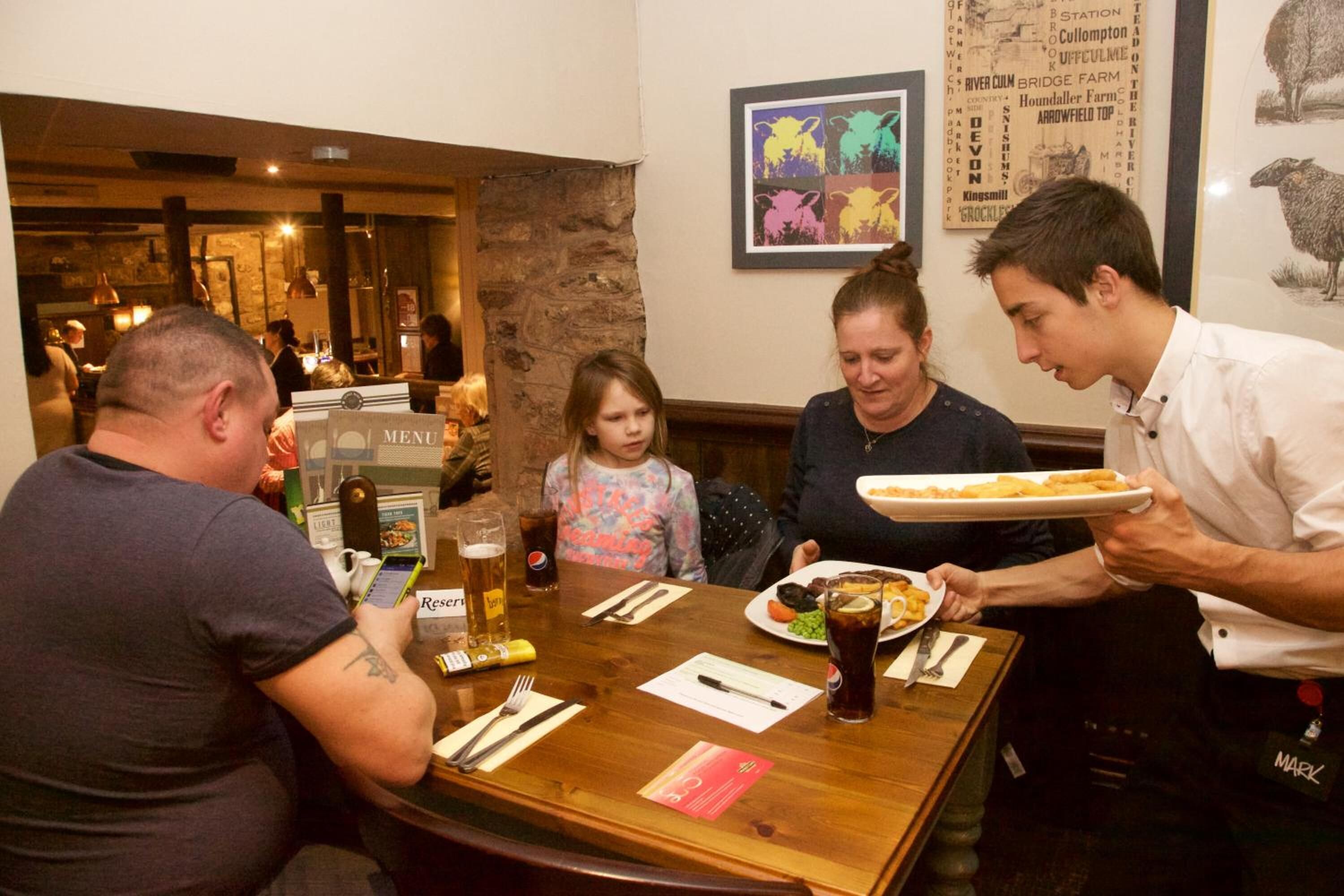 L’intérieur d’un restaurant avec une table en bois, un menu et une personne qui sert les plats.
