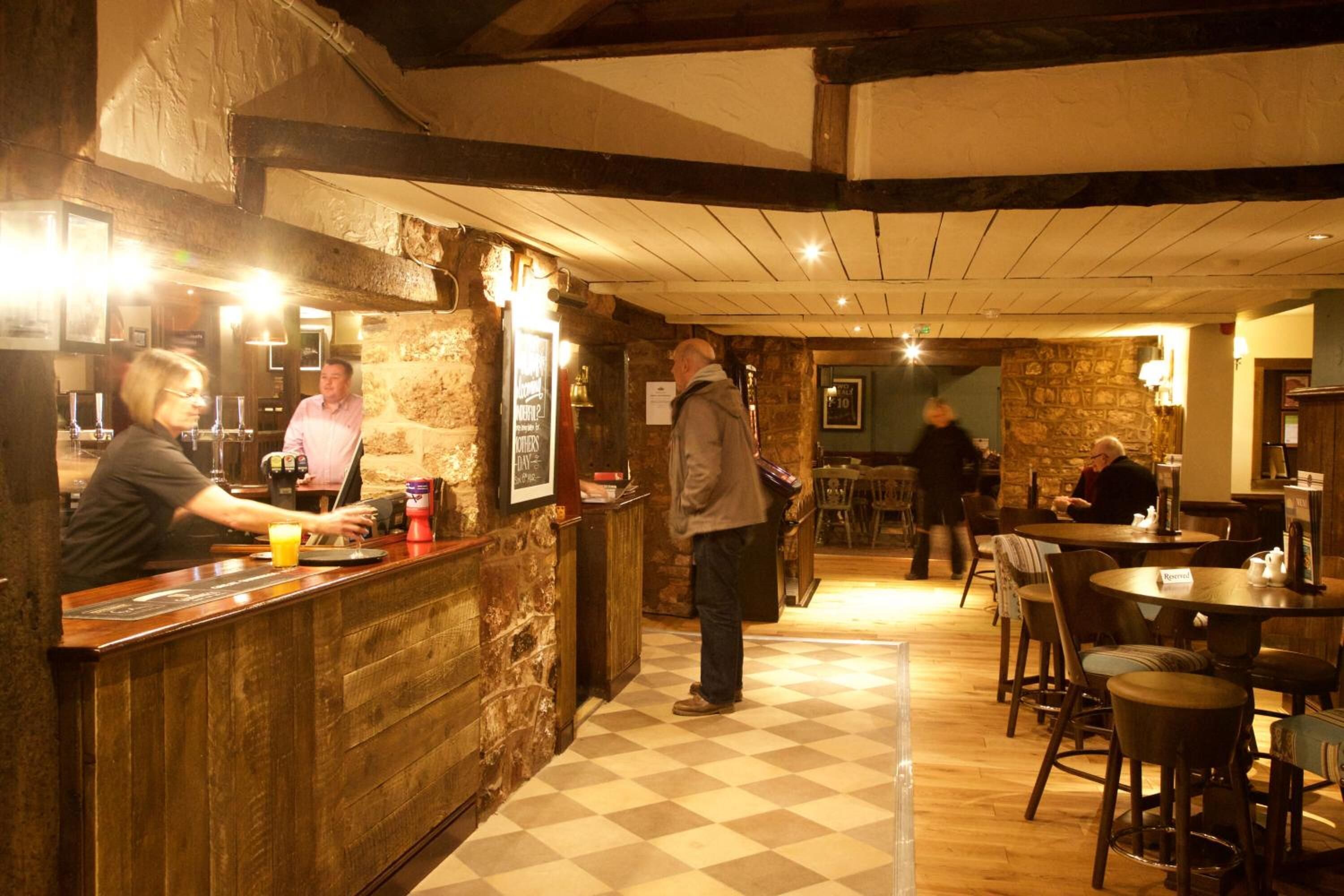 A restaurant with a wooden counter, stone walls, and checkered flooring.