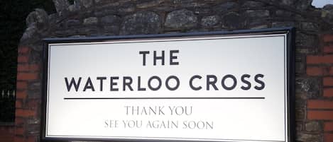 Un letrero con el texto 'THE WATERLOO CROSS' y el mensaje 'THANK YOU SEE YOU AGAIN SOON' en una pared de piedra.