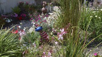 Un jardín con diversas plantas y flores, una estatua y una persona caminando al fondo.