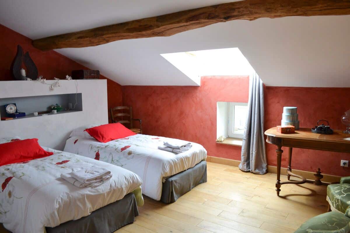 Una habitación con dos camas, una mesa de madera, una ventana con cortinas y un tragaluz.