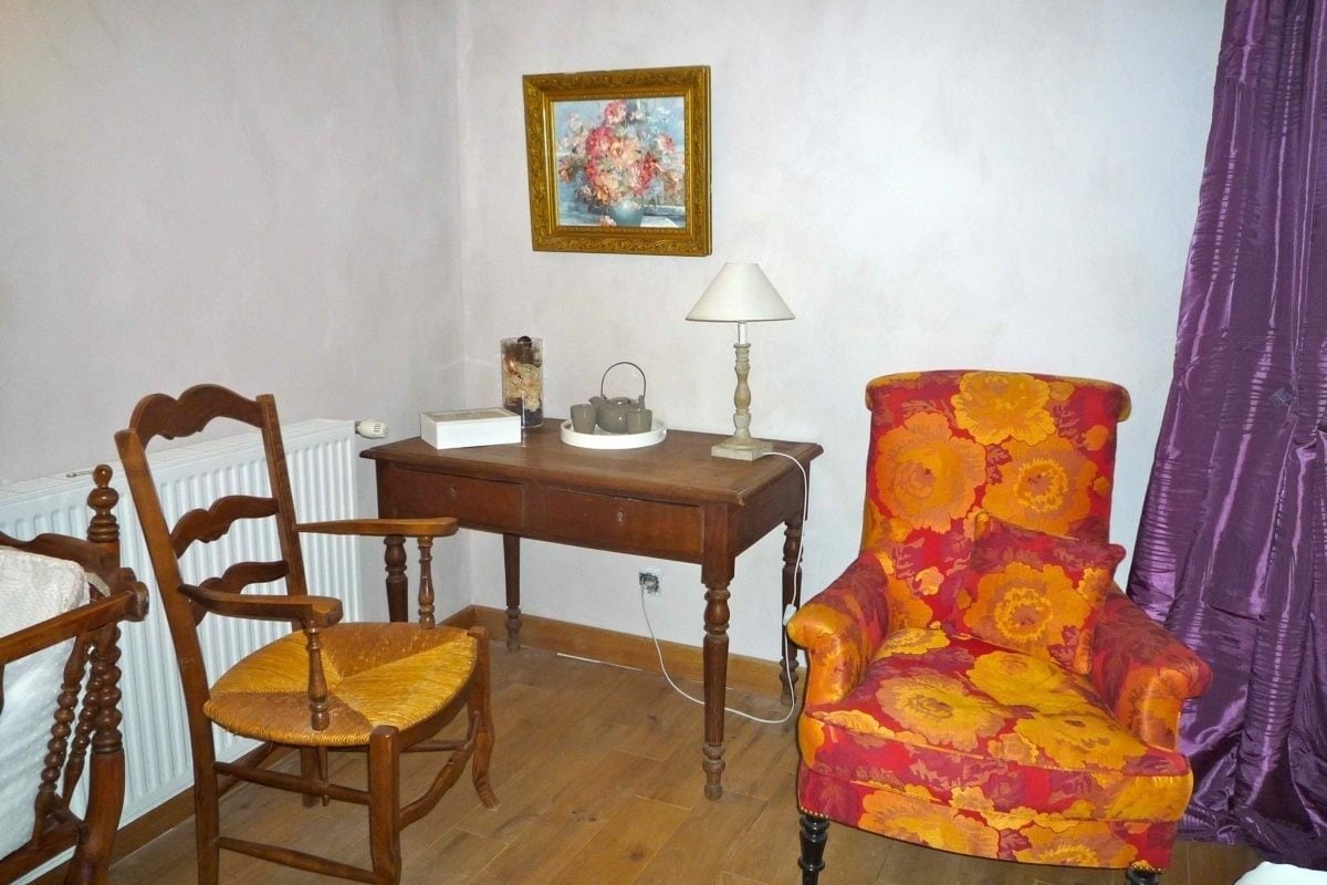 Una habitación con una silla de madera, un escritorio con una lámpara y un sillón colorido.
