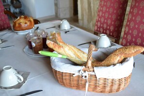 A dining table with a basket of baguettes, a loaf of bread, and several small jars of jam. - La Ferme Pateli (Courouvre)