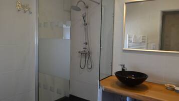 Une salle de bain dotée d’une douche à parois de verre, d’un lavabo noir et d’un miroir placé au-dessus du lavabo.