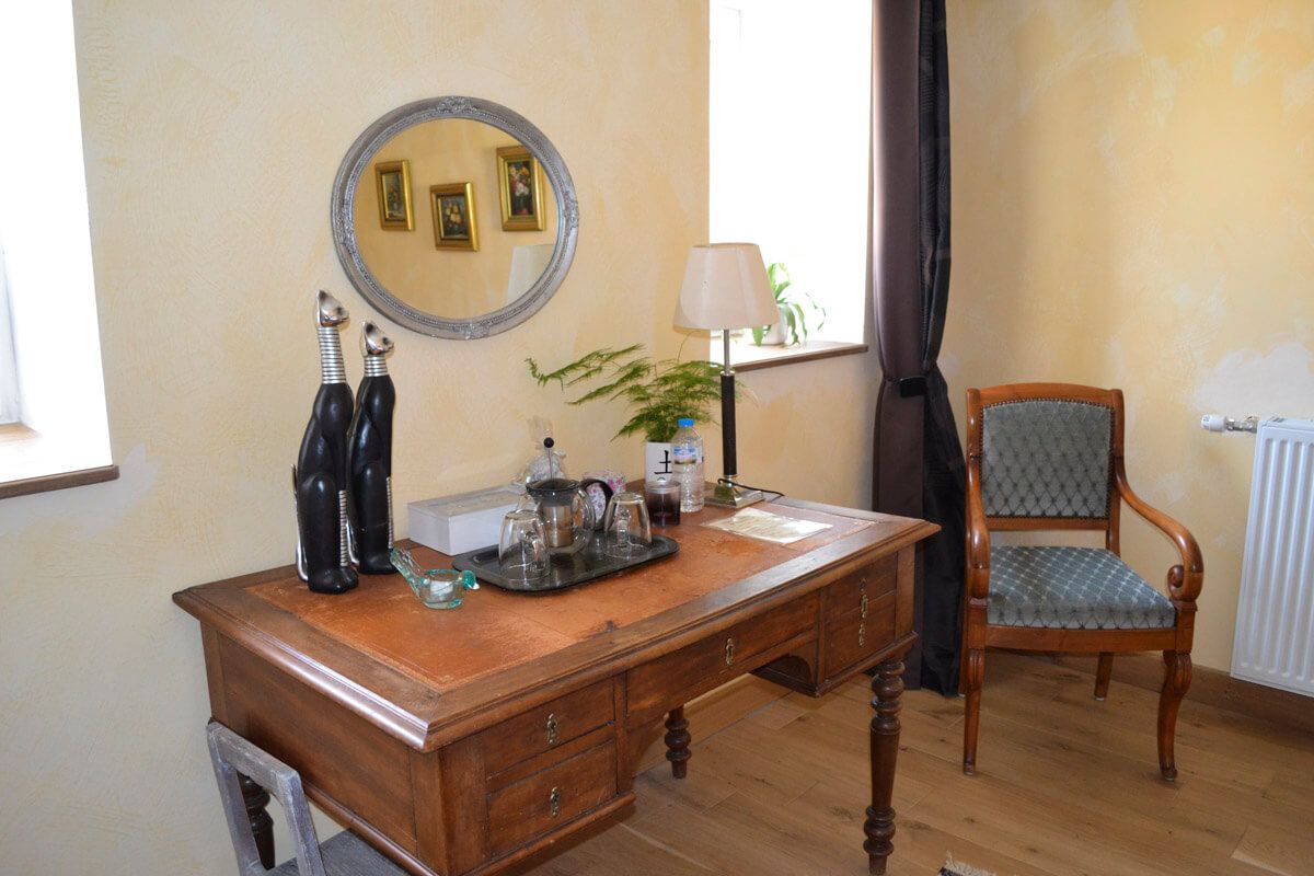 A wooden desk with a mirror, a lamp, and a chair in a room with a radiator and a window with curtains.