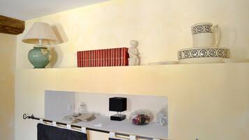 Una habitación con un escritorio, una lámpara, libros, una figura decorativa y una taza y platillo sobre una estantería.