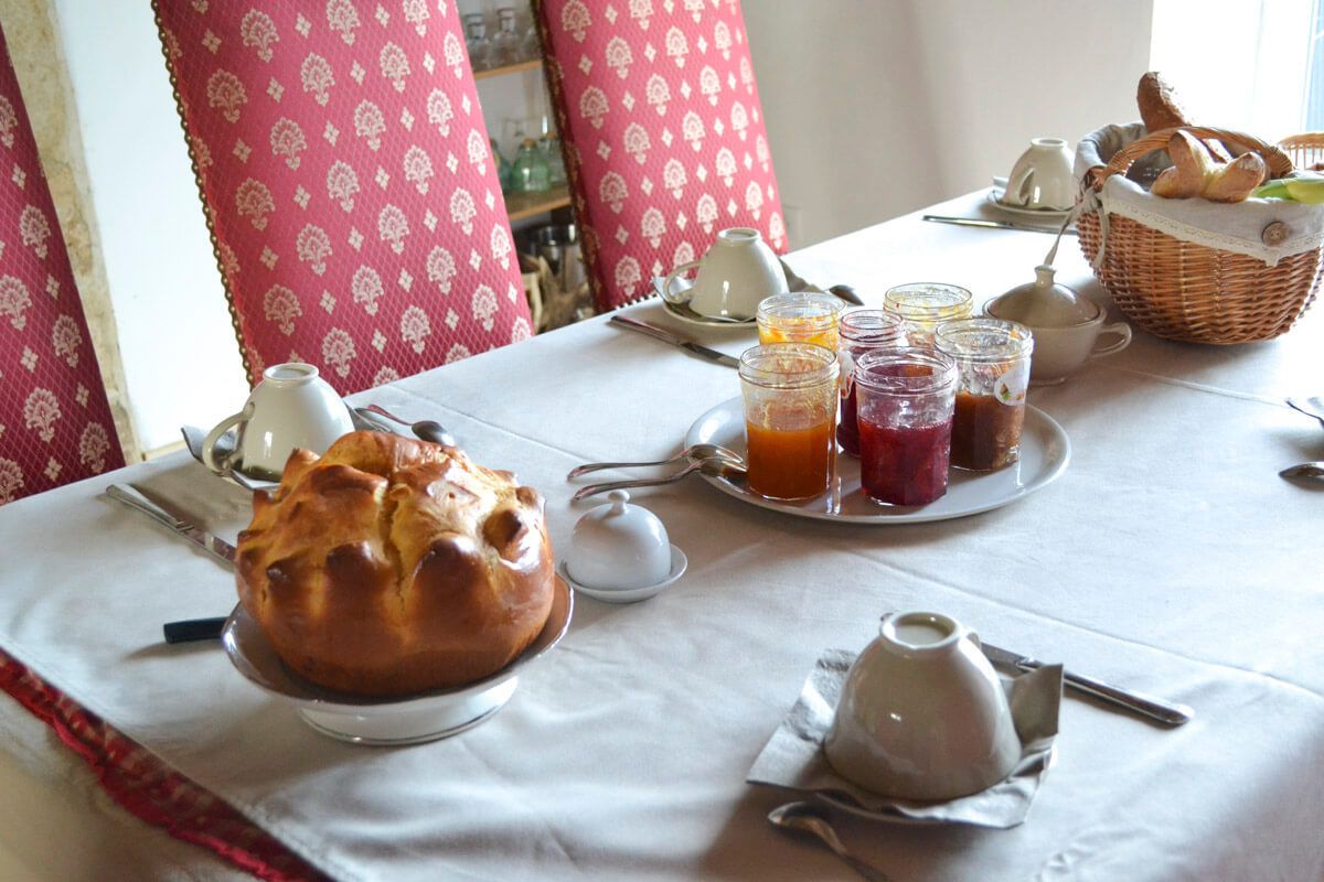 Una mesa de desayuno con pan, frascos de mermelada y una cesta de pasteles.