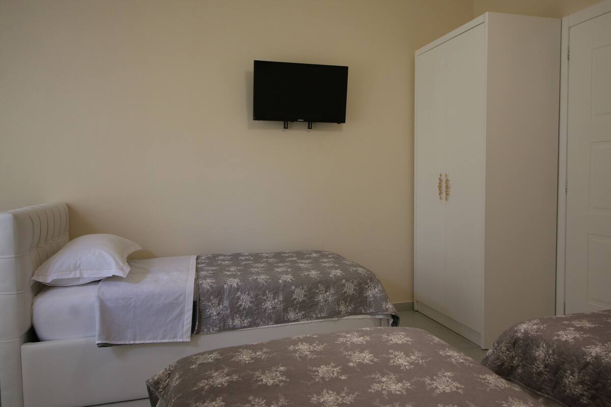 A bedroom with two beds, a wardrobe, and a television on the wall.