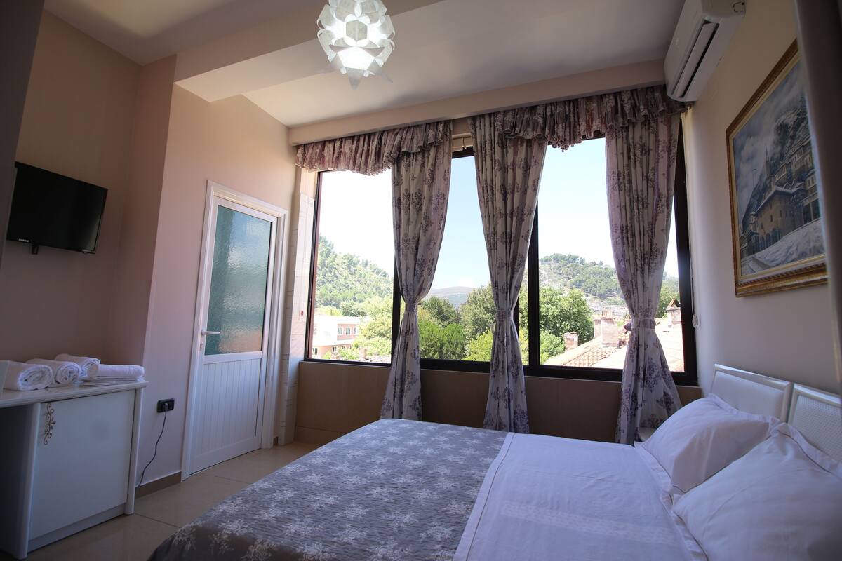 A bedroom with a bed, a dresser, a television, and a window with curtains.