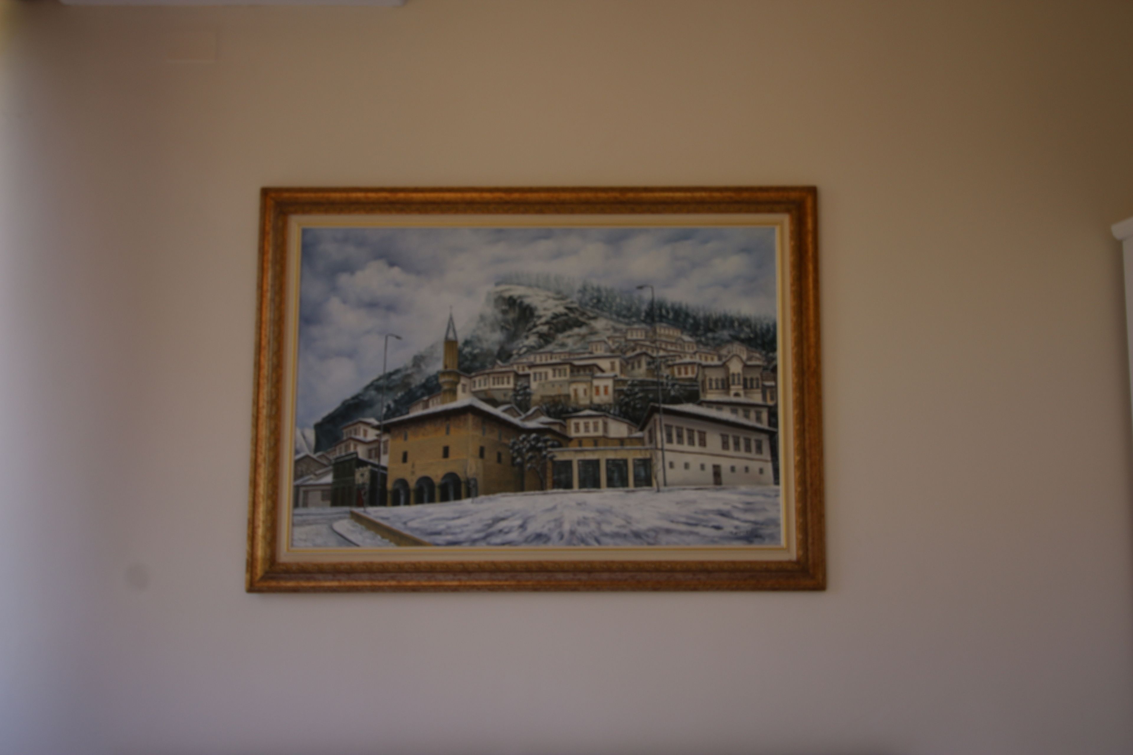 A framed painting of a snowy town with buildings and a mountain.