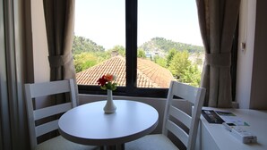 A room with a round table, two white chairs, a vase with flowers, and a window with curtains. - Hotel Orestiada (Velabisht)