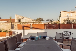 Un patio al aire libre con una mesa lista para dos personas, sillas alrededor y plantas en macetas.