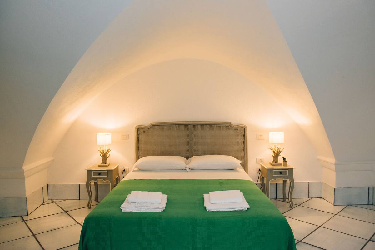 Une chambre à coucher avec un grand lit, deux tables de chevet avec des lampes et une couvre-lit verte.