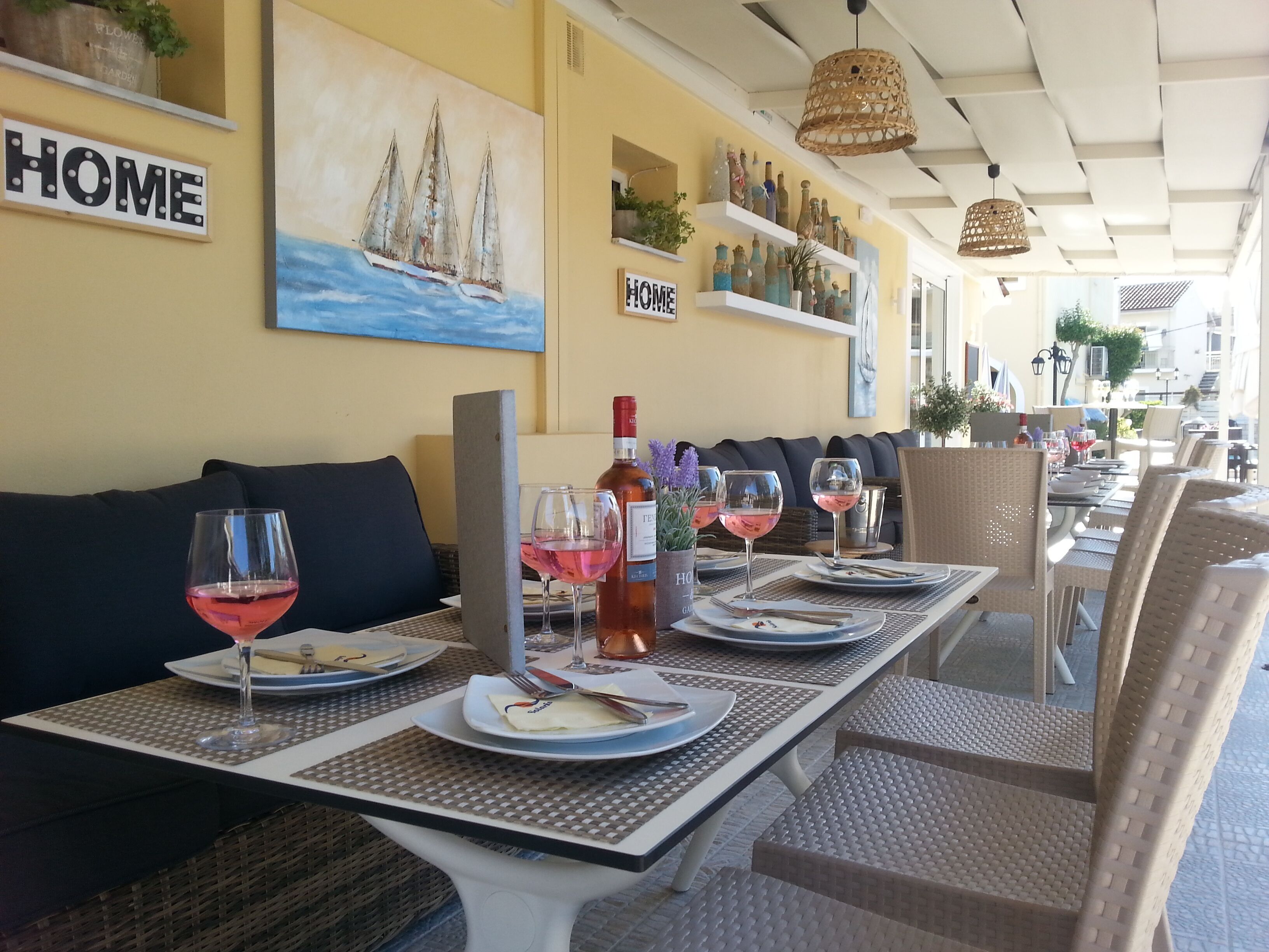 Un restaurante con terraza, mesas dispuestas con platos, vasos y una botella de vino.