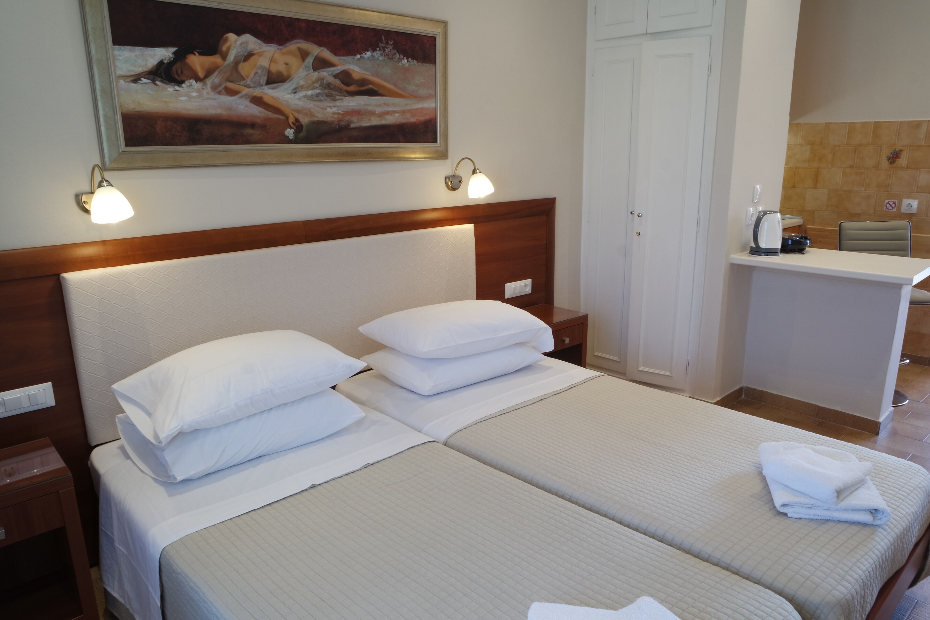 Ein Hotelzimmer mit zwei Betten, einem Bild an der Wand und einer kleinen Küchenzeile.