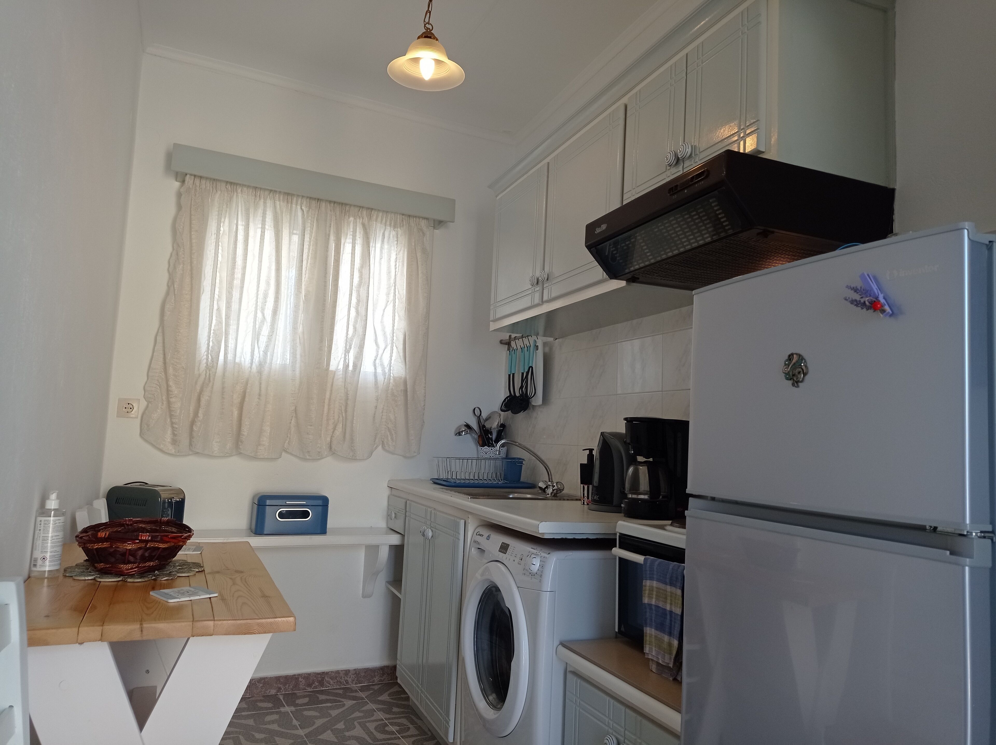 A compact kitchen with a washing machine, a coffee maker, and a refrigerator.
