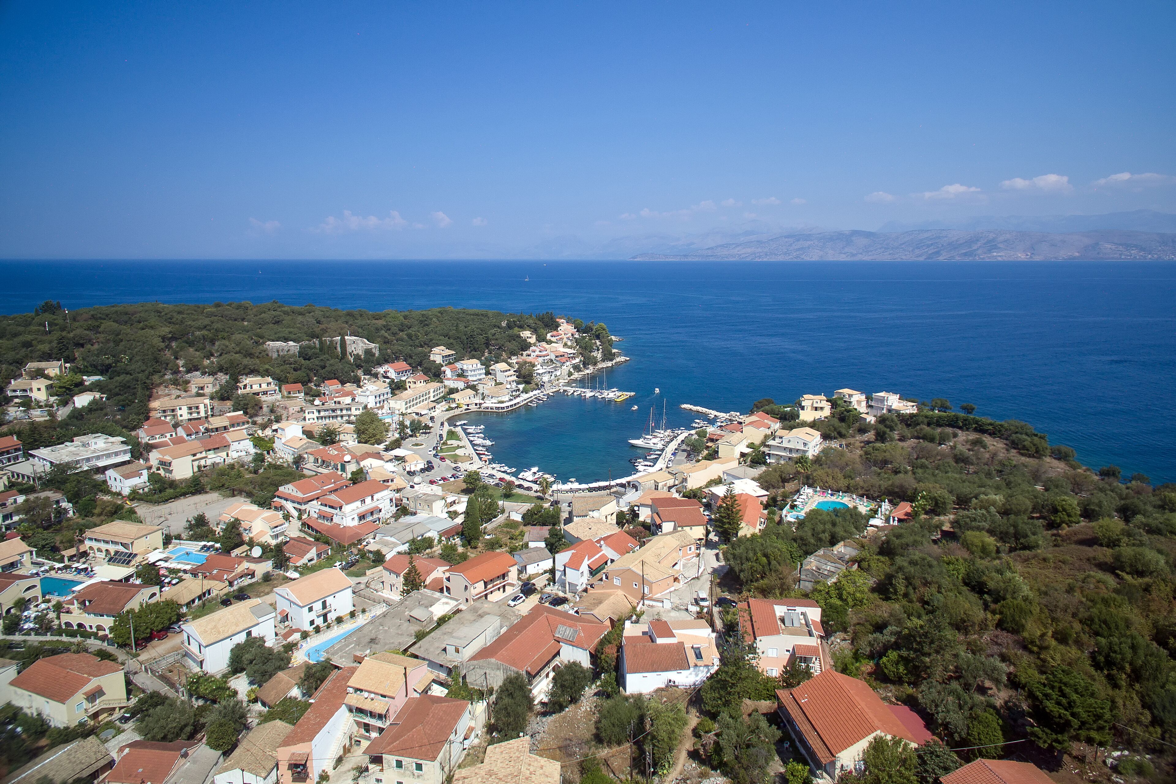 An aerial view of a coastal town with a marina, residential buildings, and a clear blue sea.