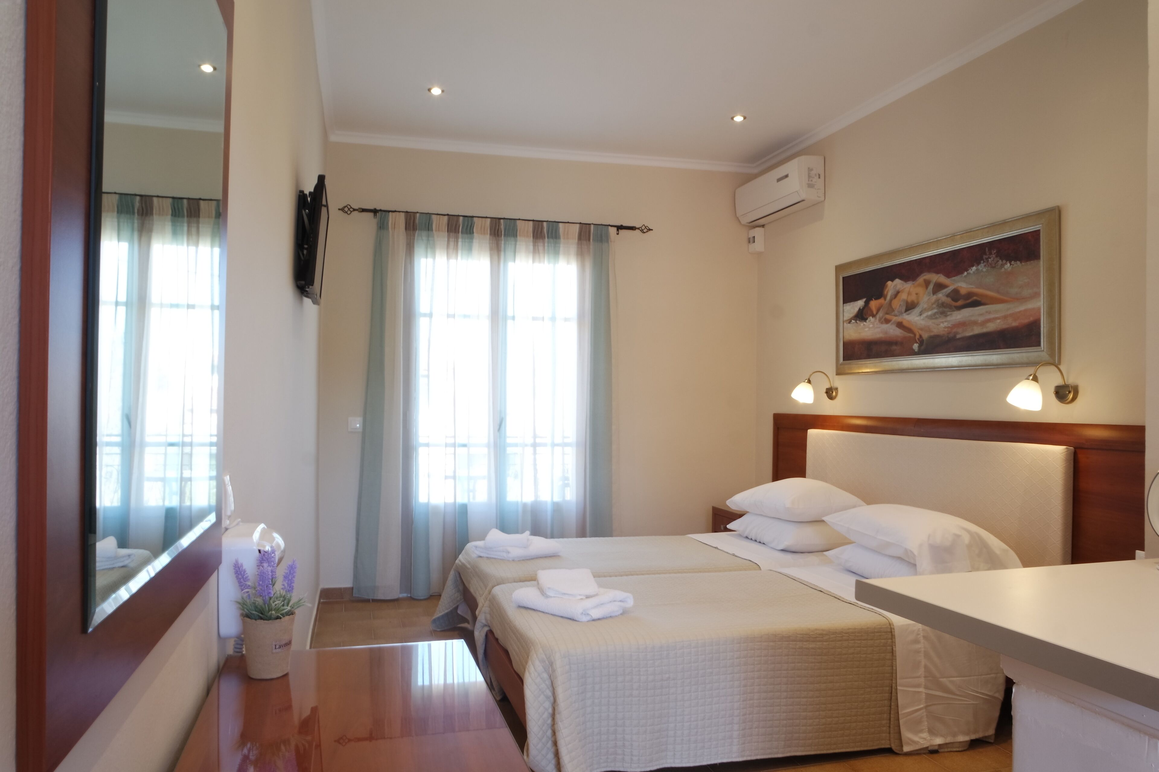 A hotel room with two beds, a large mirror, a painting on the wall, and a window with curtains.