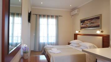 A hotel room with two beds, a large mirror, a painting on the wall, and a window with curtains.