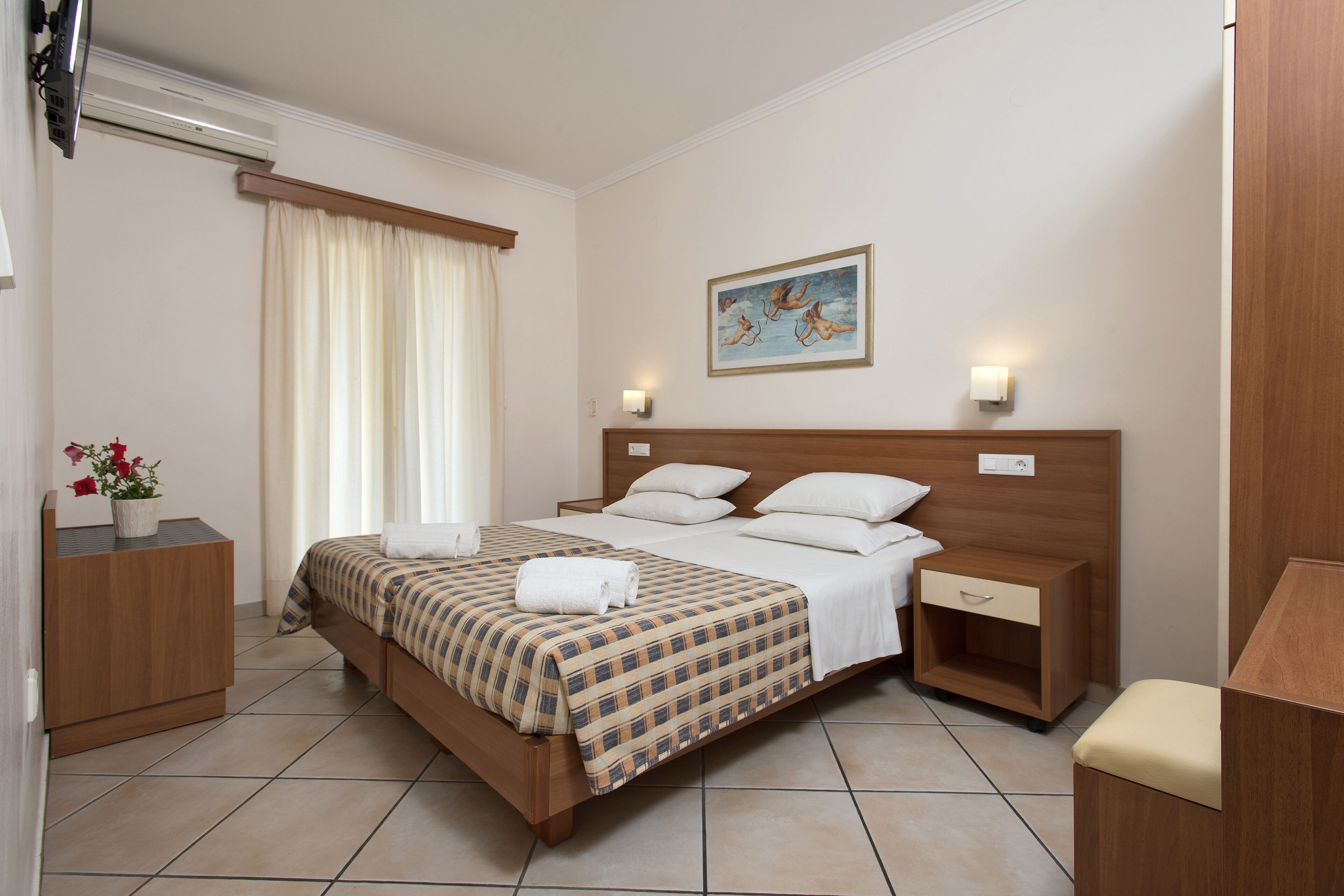 A hotel room with a bed, bedside tables, a nightstand, a chair, a painting on the wall, and a window with curtains.