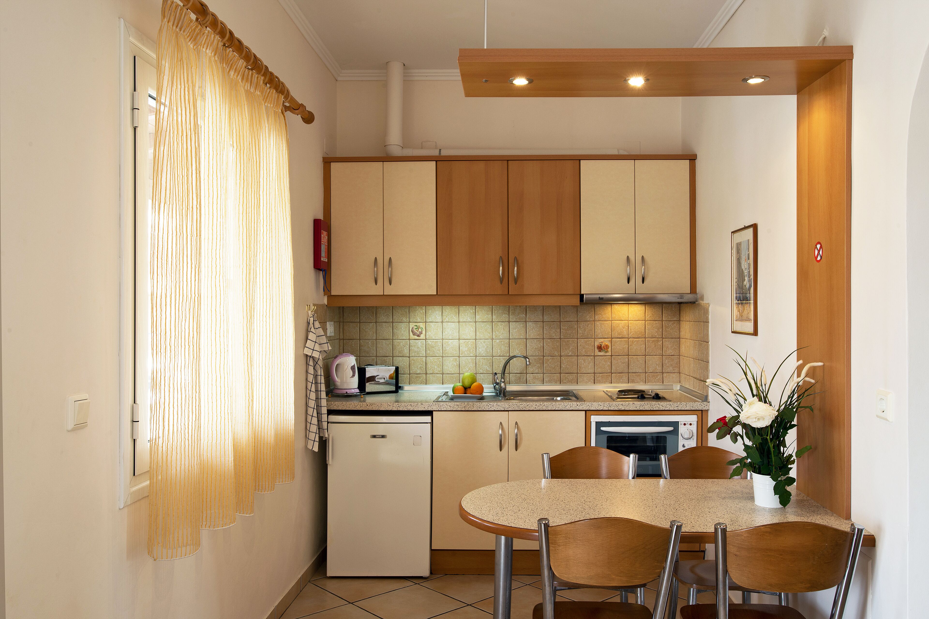 Una cocina compacta con armarios de madera, una pequeña mesa de comedor con sillas y un lavabo.