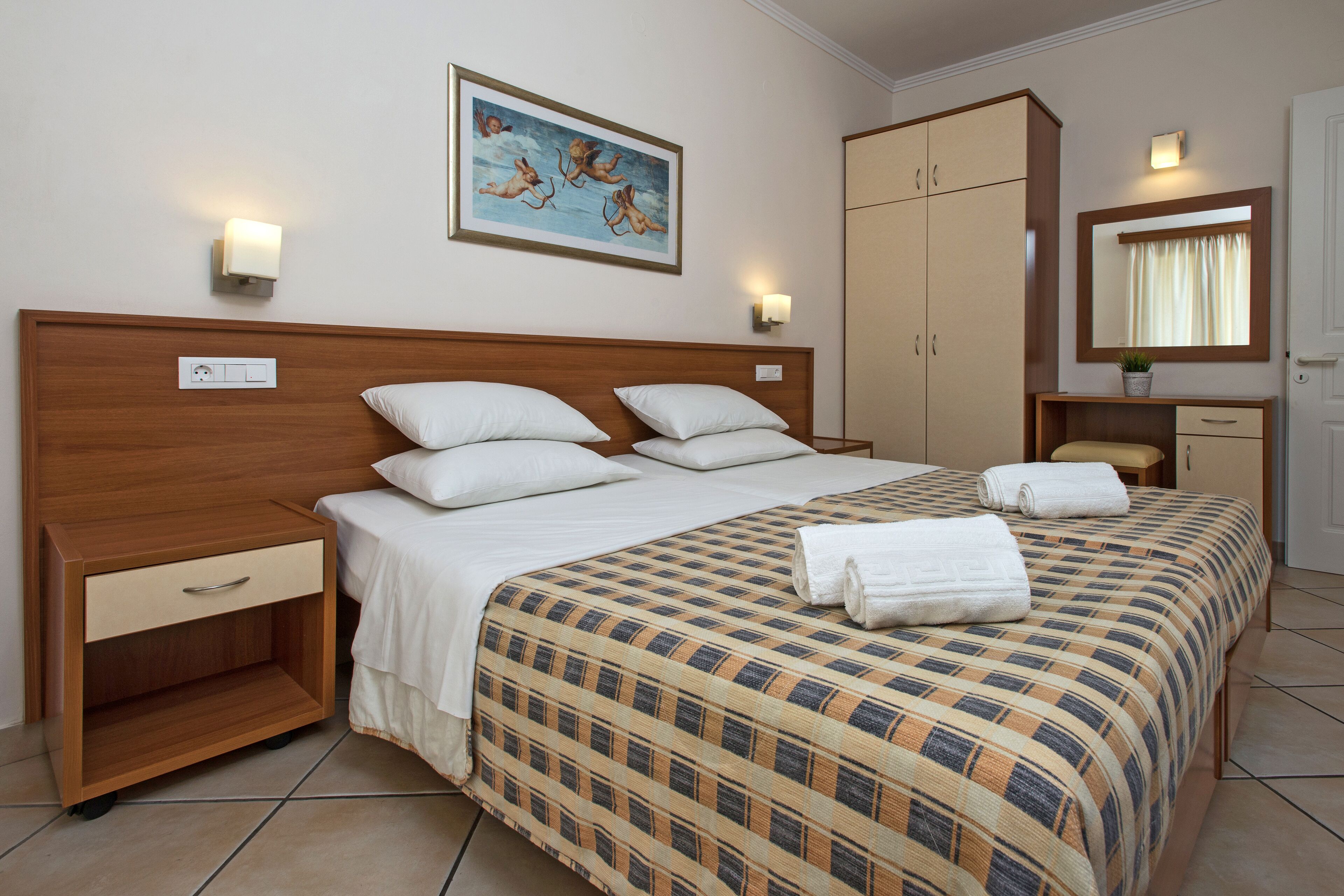 A hotel room with a large bed, a nightstand, a wardrobe, a mirror, and a painting on the wall.