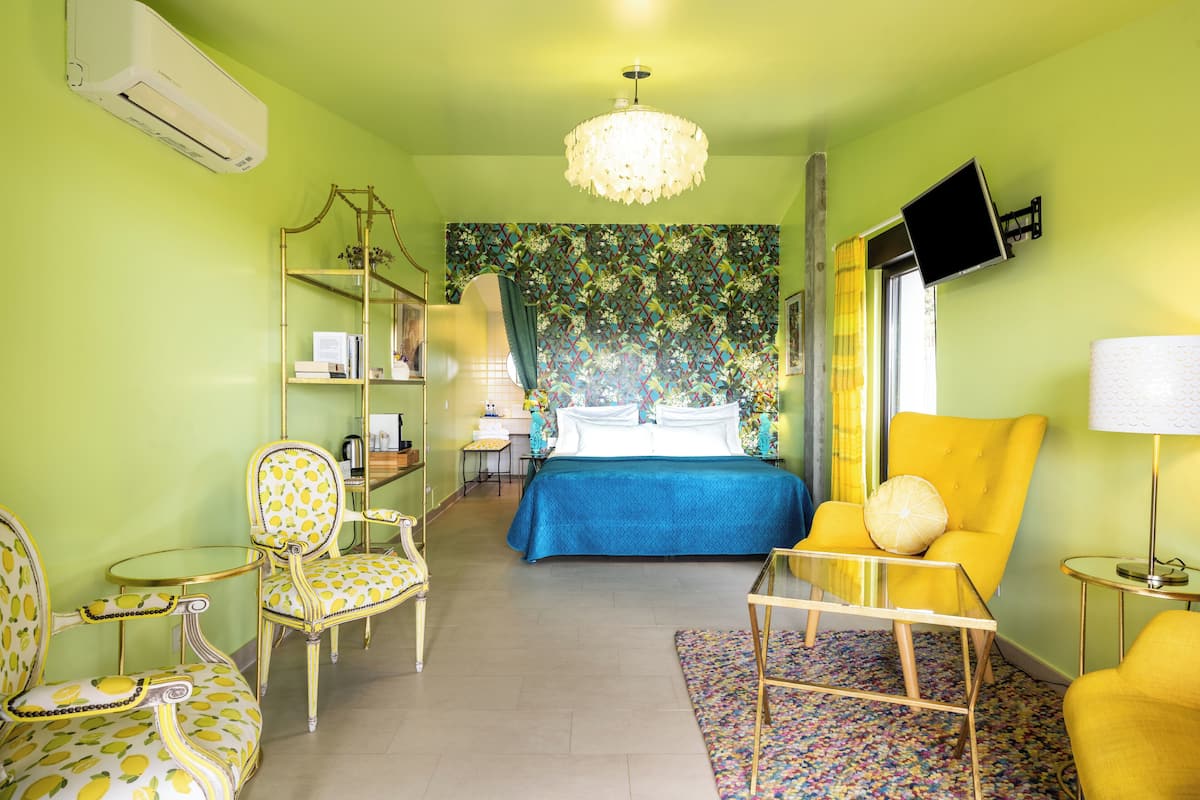 A room with a bed, a chair, a table, a lamp, and a TV on the wall.