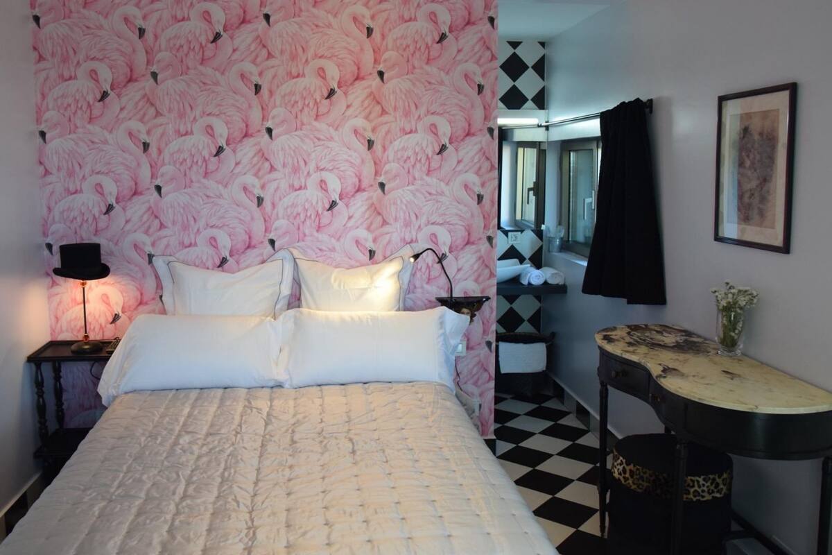 A bedroom with a bed, a nightstand, a lamp, a mirror, a dresser, and a checkered floor.