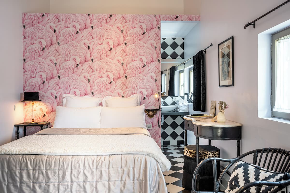 A bedroom with a bed, a nightstand, a chair, a small table, and a mirror.